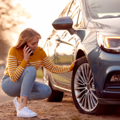 woman calling for help on phone after car breakdown on country road with tyre puncture